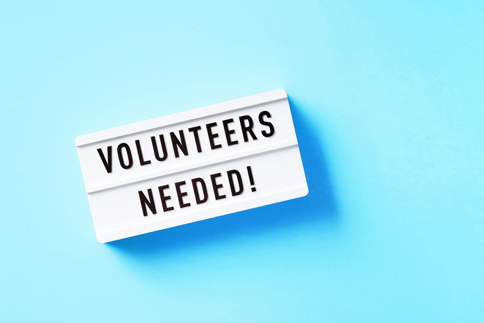 Volunteers Needed Written White Lightbox Sitting On Blue Background